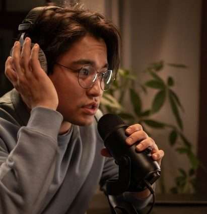 A man is leaning into a podcast microphone, he looks anxious