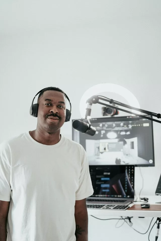 A Black man is standing up next to microphone. He is waering headphones